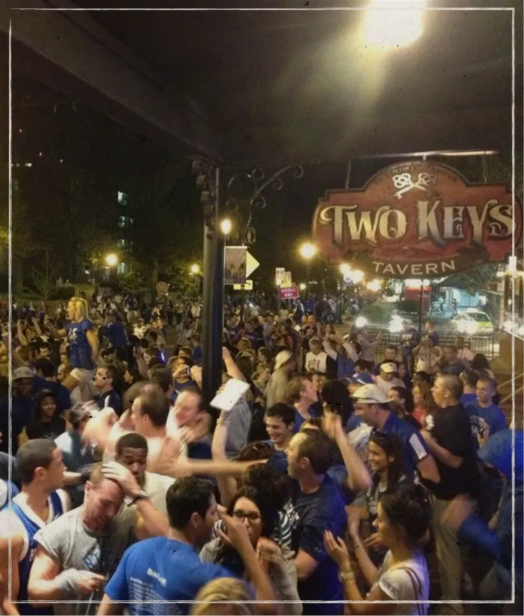 A packed crowd celebrating outside Two Keys Tavern at night.